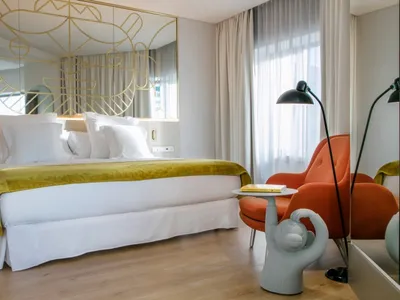 A modern bedroom featuring a bed with a white bedspread and gold metal frame, an orange upholstered armchair, and a side tabl