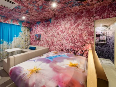 A modern bedroom with floral print walls, ceiling, and bedding, featuring a white sofa and a bed with a floral comforter.