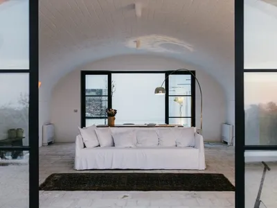 A cozy living room with a white concrete sofa, large windows, and a comfortable rug.