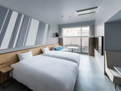 A minimalist hotel room with neutral tones, featuring two twin beds, a large window, and modern furnishings.