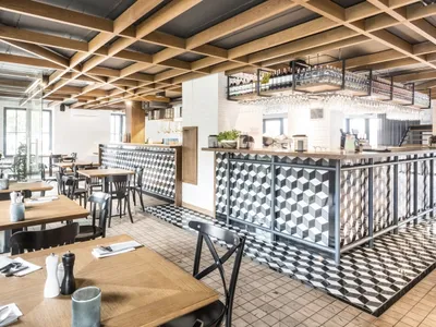 Modern restaurant interior with wooden tables, geometric-patterned tile flooring, and metallic accents.