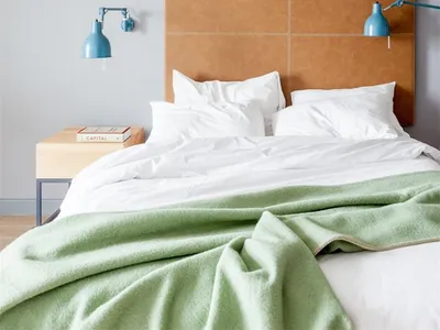 Minimalist bedroom with a bed featuring a green blanket, white sheets, and a brown leather headboard.