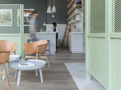 A cozy, modern restaurant/cafe interior with a light gray wooden floor, white walls, and various design elements like pendant