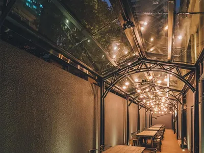 Modern, industrial-looking restaurant exterior with wooden tables, metal chairs, and glass ceiling.