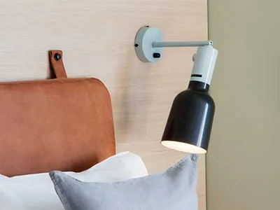 A minimalist bedroom with a gray cushion, a leather headboard, and a modern lamp on the wall.