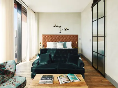 Modern bedroom featuring a green velvet sofa, a tufted leather headboard bed, and a wooden coffee table with books.