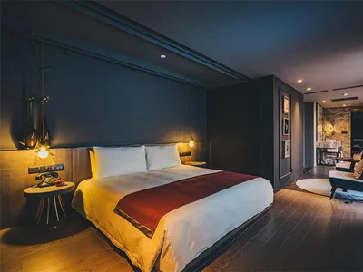Modern hotel suite with comfortable furniture, including a bed with white and red linens, a side table with a phone and plant