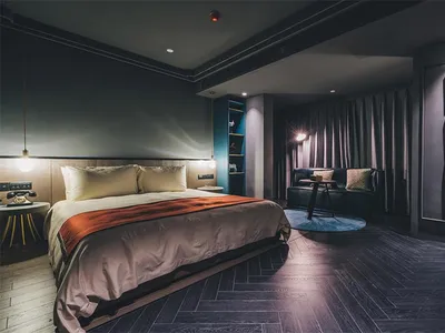 Modern hotel room featuring dark timber flooring and a comfortable bed with plush pillows and a colorful blanket.
