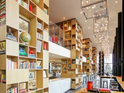 A modern restaurant bar featuring wooden furniture and shelves filled with books and globes.