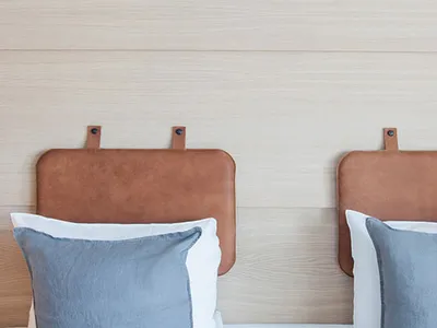 A minimalist bedroom with blue pillows on a bed, against a light-colored wooden headboard.