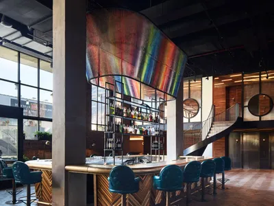Contemporary bar interior featuring modern furniture, metal accents, wood paneling, and a large, colorful suspended sculpture