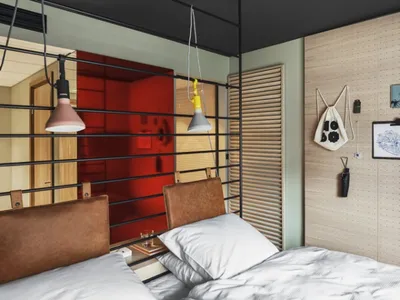 A modern bedroom featuring a leather headboard on the bed, against a red background with hanging lights and pegboard storage.