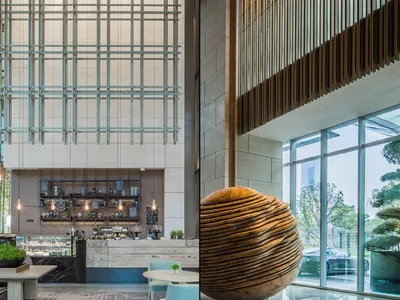 A modern hotel lobby featuring a wooden sphere sculpture and a large glass wall
