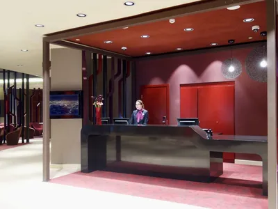 A modern hotel reception desk with a sleek design, red accent wall, and metal counter.