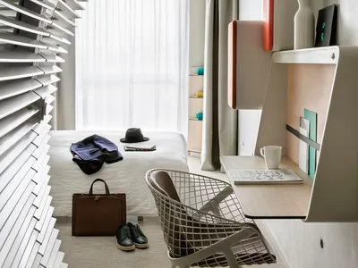 A modern minimalist bedroom with a white bed, metal chair, and minimalist design elements.