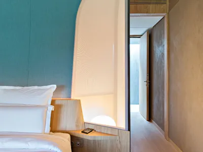 Modern minimalist bedroom featuring wooden furnishings and a fabric headboard.
