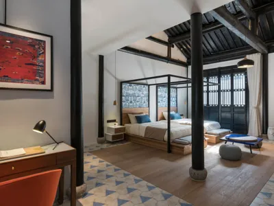 A modern bedroom featuring a desk, floor tiles with triangular patterns, and a large bed with a canopy frame.