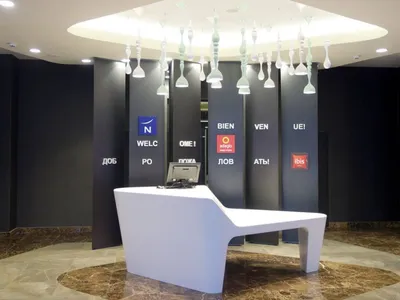 A minimalist hotel reception area with a sleek white desk, black walls, and modern light fixtures.