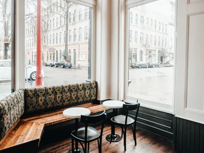 A cozy cafe corner featuring detailed windows, comfortable seating, and a rustic floor, with a view of the street.