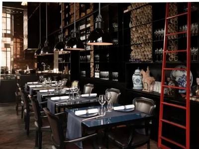 A modern industrial restaurant interior featuring metal pendant lights, wooden chairs, and glassware.