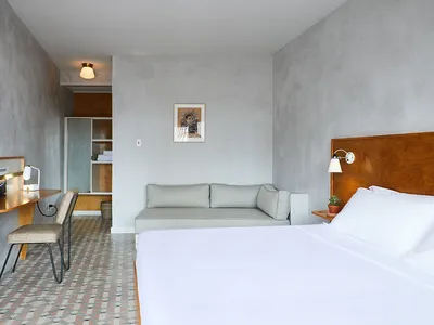 Modern minimalist bedroom featuring concrete walls and floor, a white bed, and a grey couch.