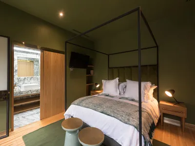 A modern, minimalist bedroom featuring a four-poster bed, wooden flooring, and green walls.