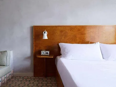 A minimalist bedroom featuring a wooden headboard with white bedding and a cozy corner sofa.