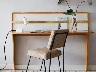 Minimalist home office workspace featuring a wooden desk with brass accents, a comfortable upholstered chair, and decorative