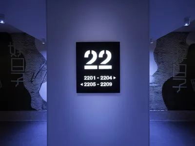 A minimalist hotel room directory with numbered rooms and directional signs, mounted on a metal panel.