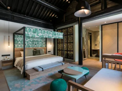 Modern bedroom in a converted barn with wooden beams, a green and white bed canopy, and a minimalist design