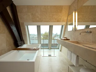 Modern bathroom with a white freestanding bathtub, a large marble sink vanity, and a large window providing a city view.