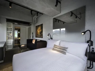 Modern bedroom with minimalist design, featuring concrete walls and white bedding.