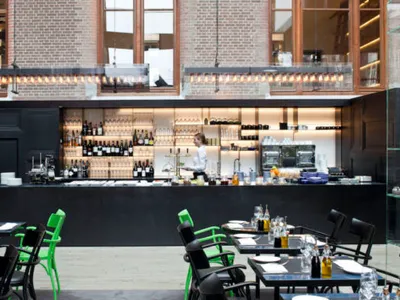 Interior design of a modern restaurant featuring a bar area with black countertops, wine bottles, and green chairs.