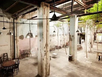 Industrial-style restaurant interior with concrete floors, steel columns, and glass pendant lights.