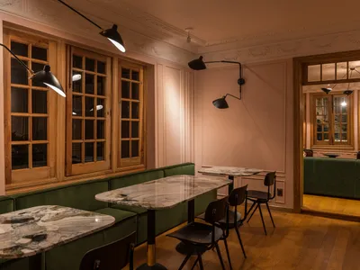 Interior of a modern cafe with marble tables, green upholstered seating, and wooden floors.