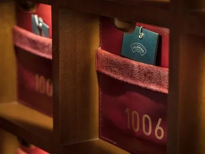 Hotel room number tags displayed on a wooden and leather wall storage unit.