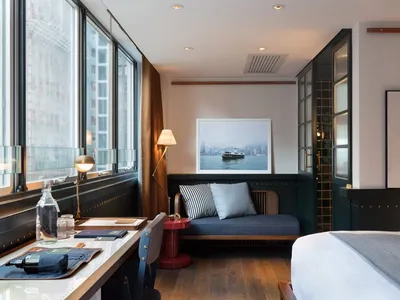 Industrial-style hotel room featuring modern furniture, wooden floors, and a large window.