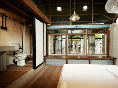 Minimalist bedroom with wood flooring and furnishings, featuring a bed and bathroom area.