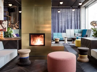 A modern hotel lounge with a fireplace, contemporary seating, and metallic, wooden, and concrete decor.
