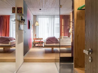Modern hotel suite with wooden flooring and furniture, minimalistic design, and large windows.