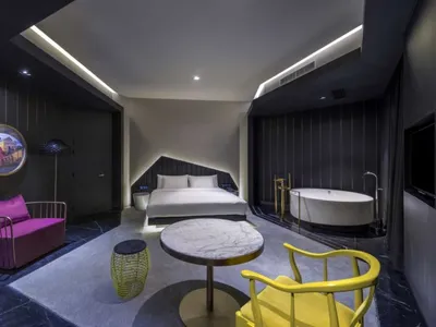 Modern minimalist bedroom with concrete walls, a white bed, and a yellow armchair.