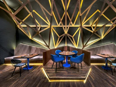 A modern restaurant dining room featuring geometric metal wall art, wooden seating, and warm lighting