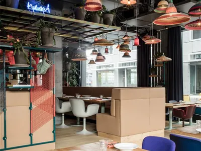 A modern restaurant interior with wooden tables, fabric chairs, and metal accents.