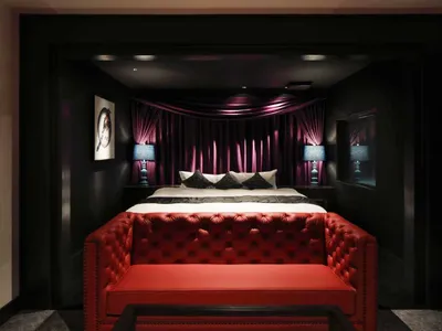 Modern minimalist bedroom featuring a red sofa, blue lamps, and a backlit curtain.