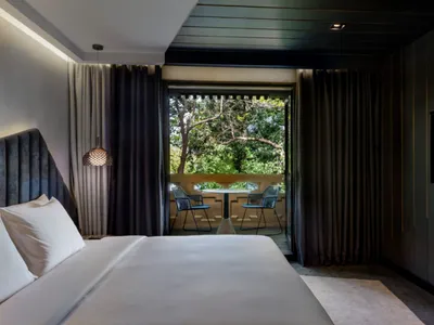 Clean, well-designed minimalist bedroom with grey curtains, a bed with a grey headboard, a small table with two chairs on a b
