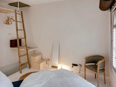 A minimalist bedroom featuring wooden furniture and white walls, with a ladder leading to a loft area.