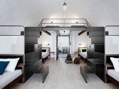 A minimalist hotel room with black, white, and wood accents and a metal loft bed.