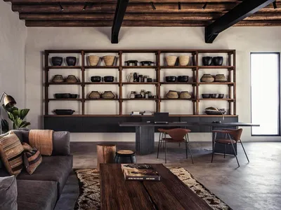 A modern industrial living room featuring wooden shelves, a gray sectional sofa, and a concrete floor.