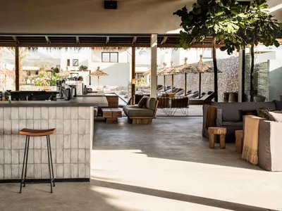 Concrete restaurant bar with stools, exposed brick wall, and outdoor seating area with umbrellas and lounge chairs.