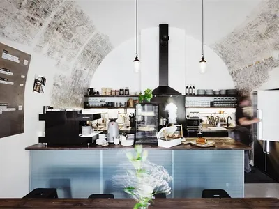 A modern coffee shop interior with concrete walls, a wooden counter, and industrial pendant lights.